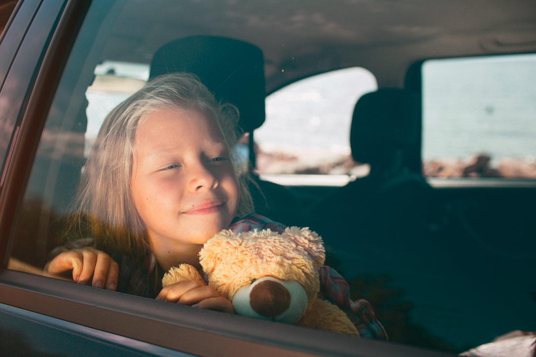 Kind mit Teddybär schaut aus dem Autofenster