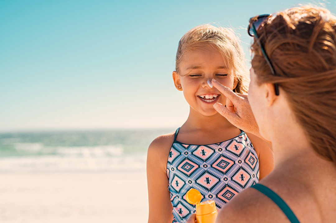 Mutter cremt ihre Tochter am Strand mit Sonnencreme ein.