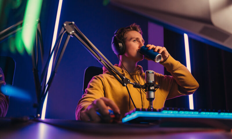 jugendlicher sitzt vor rechner und spielt videospiele waehrend er einen energy drink trinkt