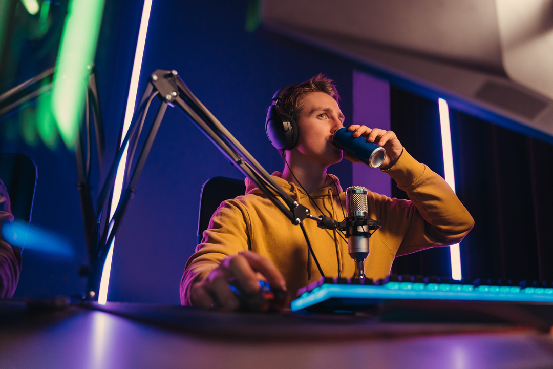 jugendlicher sitzt vor rechner und spielt videospiele waehrend er einen energy drink trinkt