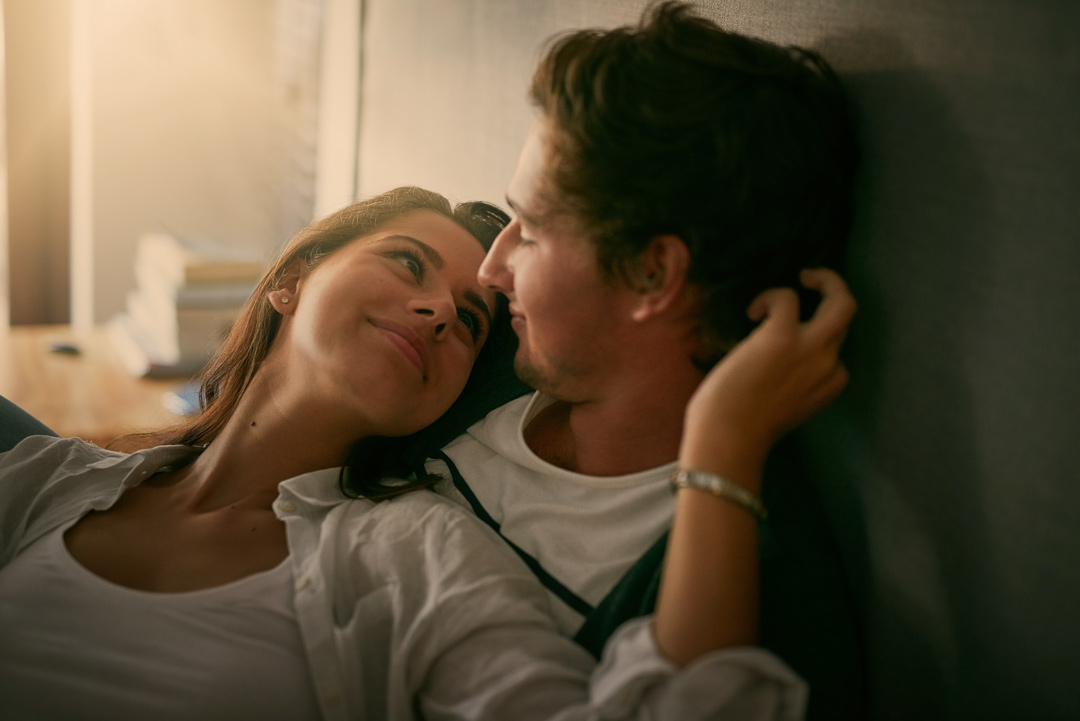 frau und mann liegen gemeinsam im bett und frau schmiegt sich liebevoll an ihn und schaut ihm in die augen