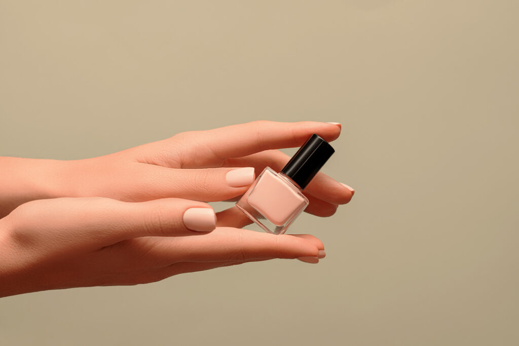 eine hand mit lackierten naegeln haelt ein flaeschchen mit nagellack