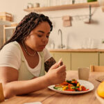 frau sitzt an tisch uns isst nachdenklich ihr essen